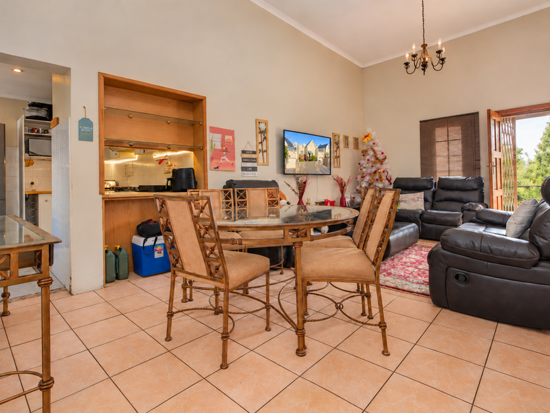 Open-plan living and dining area featuring tiled flooring, a built-in kitchen nook, and direct access to an outdoor balcony through a security gate.