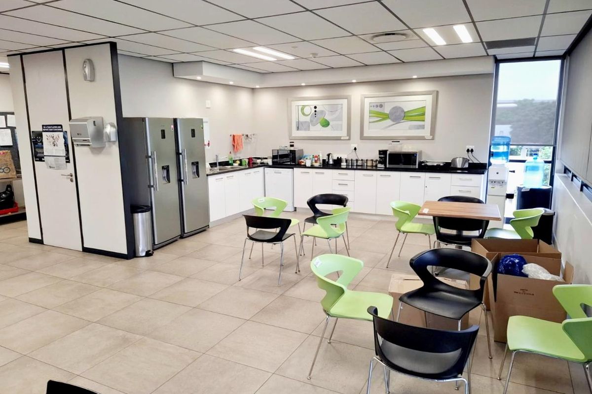 A functional office breakroom featuring a kitchenette with white cabinetry, dark countertops, tiled flooring, and a suspended ceiling with recessed lighting.
