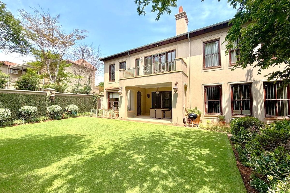 Rear view of a two-story house featuring a covered patio, upper-level balcony, security bars on windows, and a well-maintained lawn and garden.