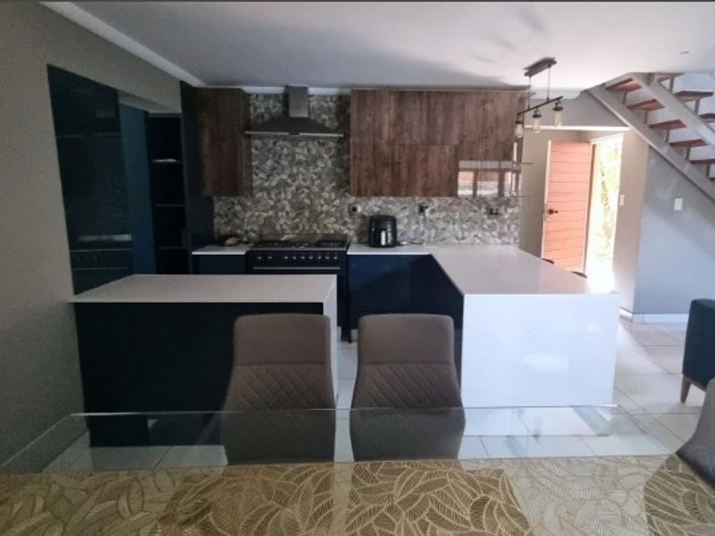 Modern open-plan kitchen featuring dark cabinetry, stone countertops, gas stove, and a tiled backsplash, seamlessly integrated with the living area and staircase.