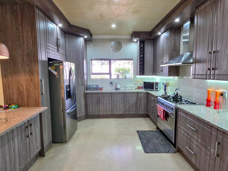 Modern kitchen featuring wood-grain cabinetry, granite countertops, stainless steel appliances, and integrated under-cabinet lighting.