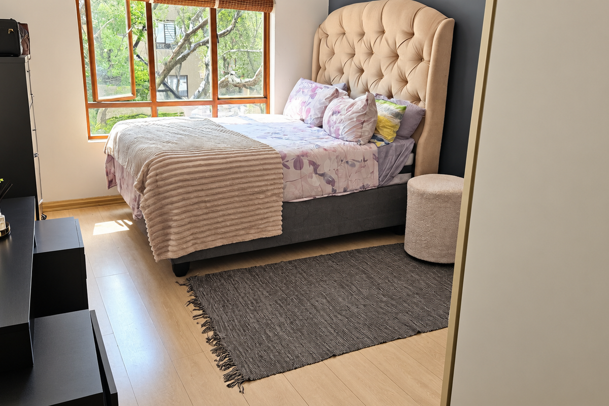 A well-lit bedroom featuring light-toned laminate flooring, a large timber-framed window, and a built-in wardrobe.