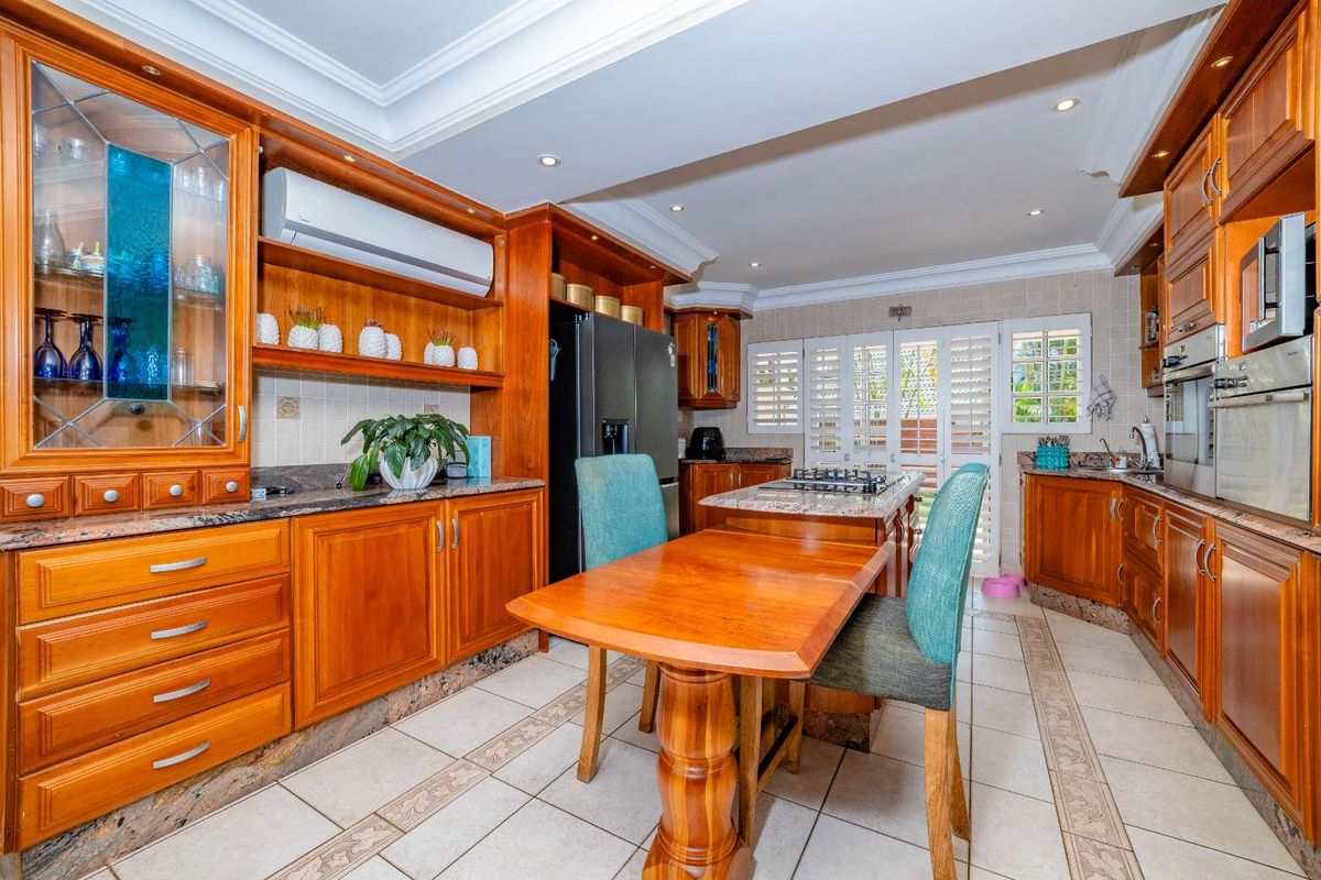 Spacious kitchen featuring warm wooden cabinetry, granite countertops, built-in appliances, and tiled flooring, with direct access to the outdoor area through plantation shutters.