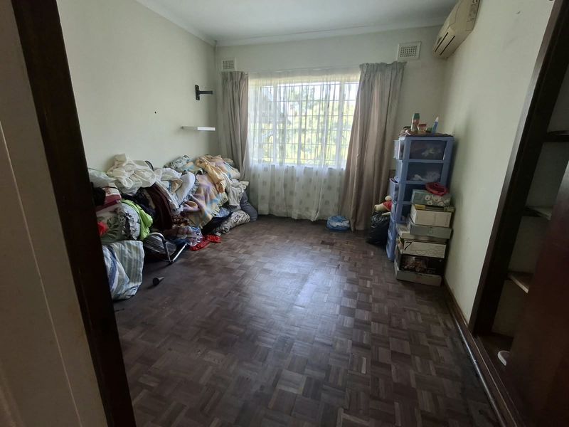 A bedroom featuring parquet flooring, an air conditioning unit, and security bars on the window, offering a functional space with potential for cosmetic updates.