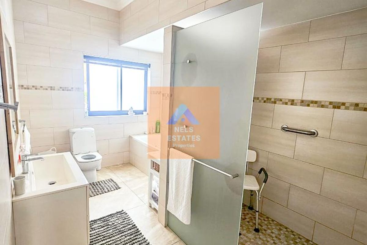 Modern bathroom featuring a walk-in shower with glass screen, wall-mounted vanity, toilet, and neutral floor-to-ceiling tiling.
