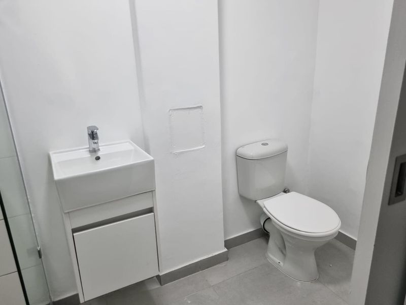 A clean, minimalist bathroom featuring a modern vanity with basin, mixer tap, and a standard toilet on tiled flooring.