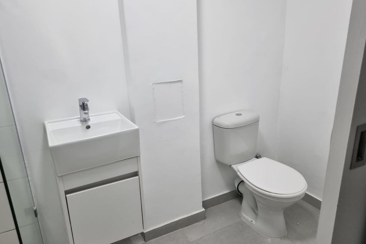 A clean, minimalist bathroom featuring a modern vanity with basin, mixer tap, and a standard toilet on tiled flooring.