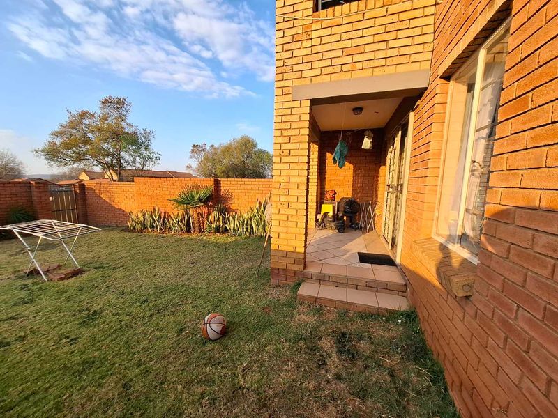 A rear view of the apartment featuring a brick facade, a small tiled patio area, and a private garden enclosed by a brick boundary wall.
