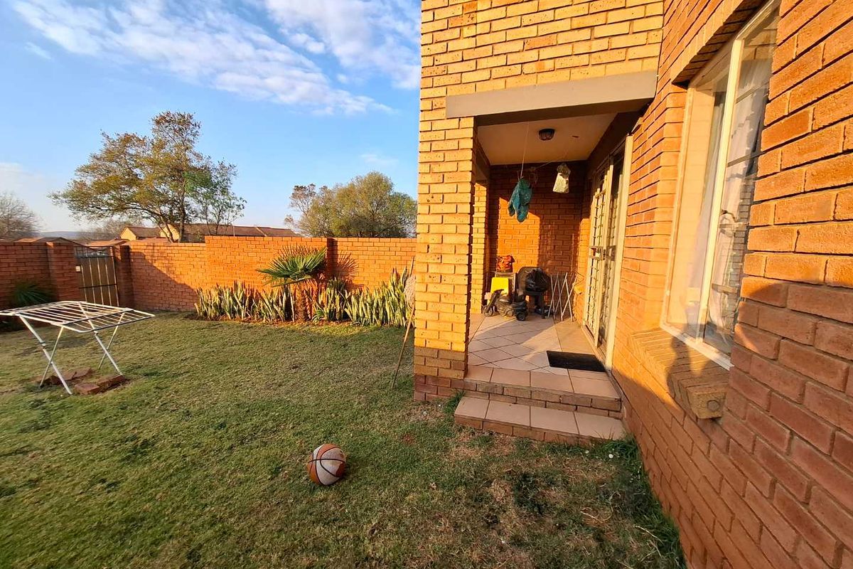 A rear view of the apartment featuring a brick facade, a small tiled patio area, and a private garden enclosed by a brick boundary wall.