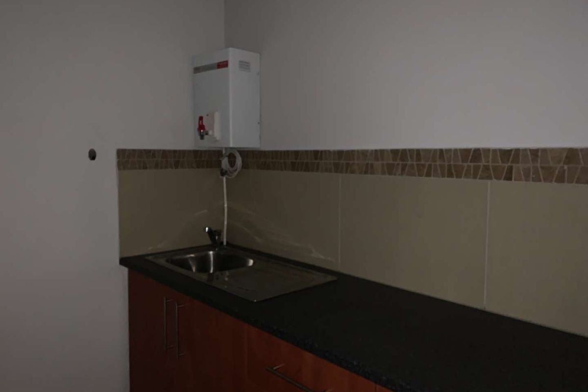 A compact kitchenette area featuring built-in cabinetry, a stainless steel sink, tiled backsplash, and an installed electric water heater.