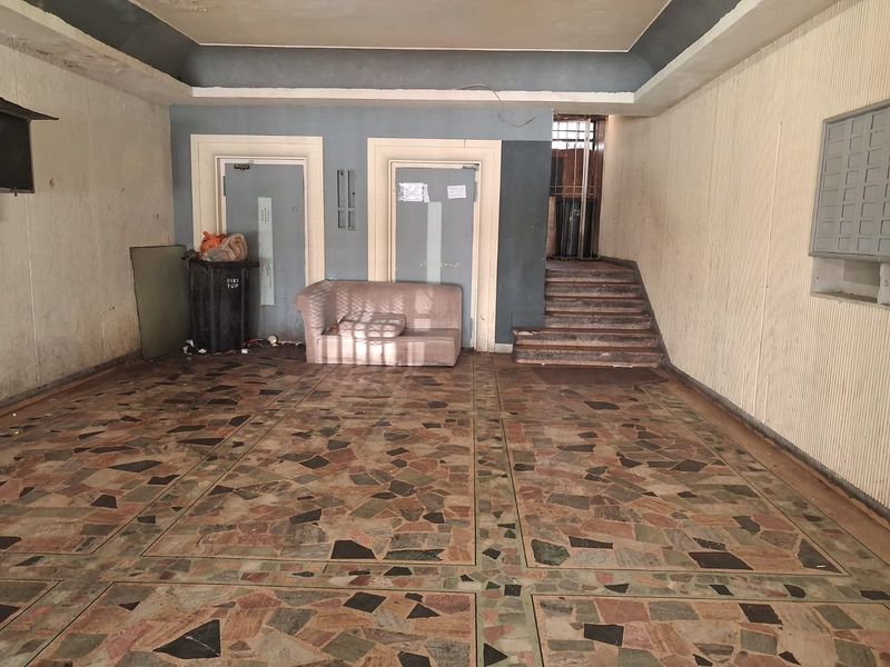 A dated apartment building entrance lobby featuring terrazzo flooring, elevator access, and a staircase, currently in need of cosmetic refurbishment.