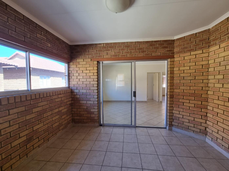An enclosed patio area featuring exposed brick walls, tiled flooring, and a sliding glass door leading into the main living space.