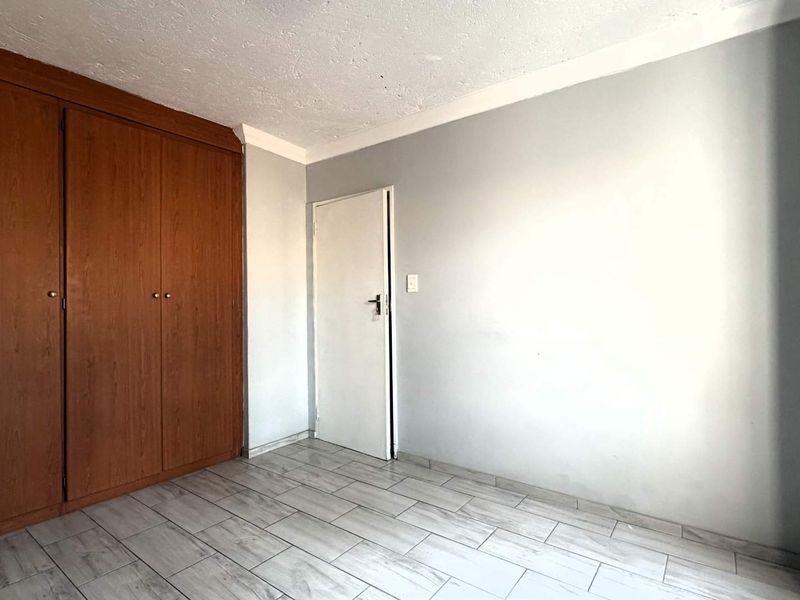 A vacant bedroom featuring tiled flooring, a built-in wooden wardrobe, and neutral wall finishes.