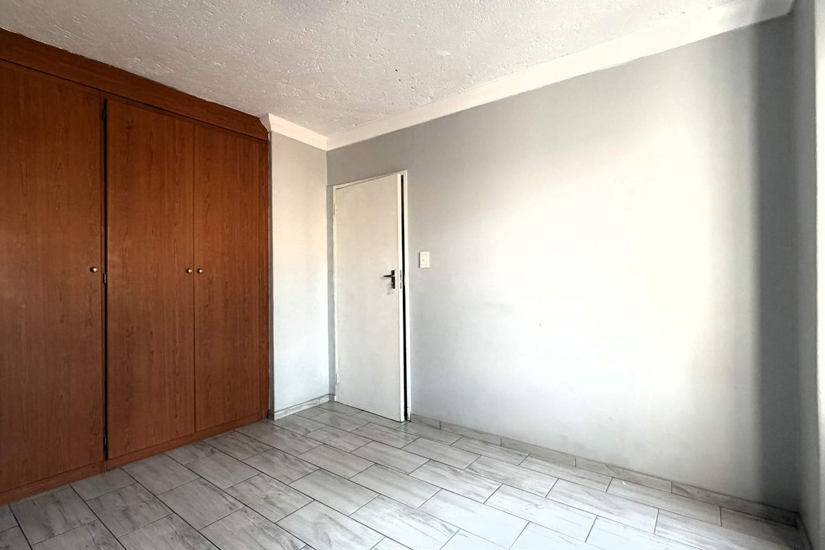 A vacant bedroom featuring tiled flooring, a built-in wooden wardrobe, and neutral wall finishes.