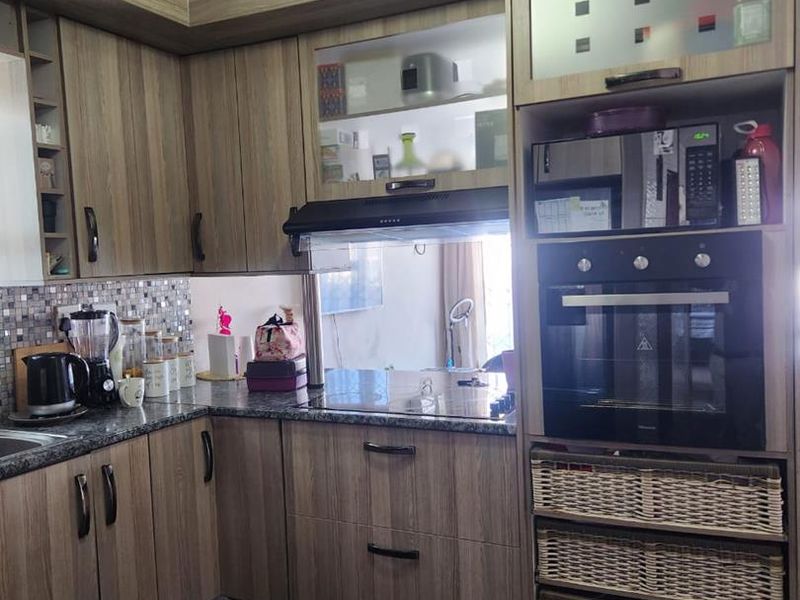 A functional kitchen featuring wood-look laminate cabinetry, built-in oven, extractor fan, mosaic tile backsplash, and granite countertops.