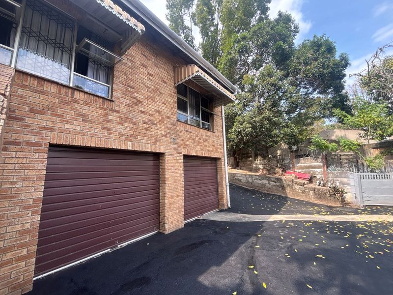 Exterior view of a brick house featuring a double garage, asphalt driveway, and window awnings with security bars.