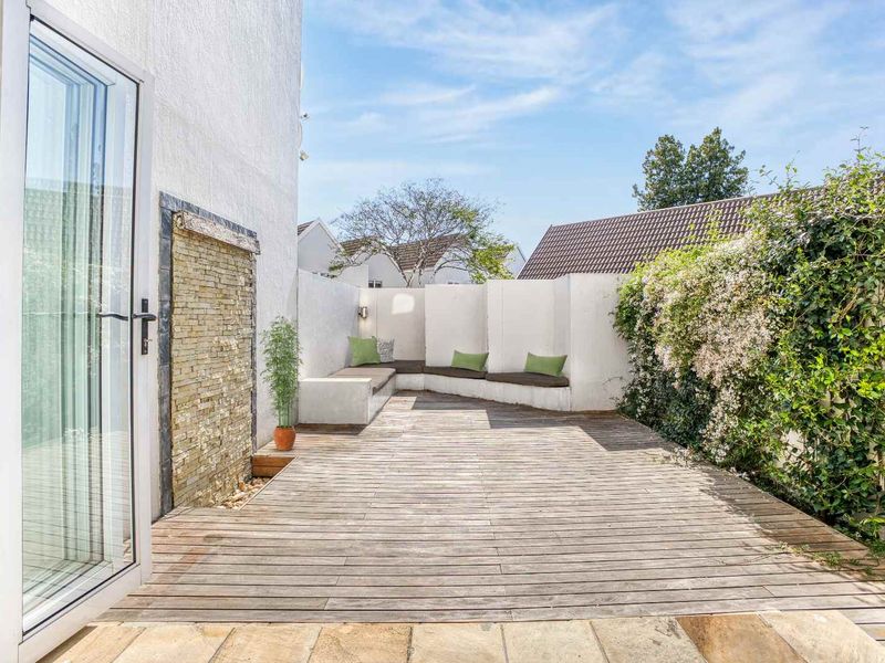 A private outdoor patio featuring timber decking, a built-in bench seating area, and a decorative stone feature wall, accessible via double french doors.