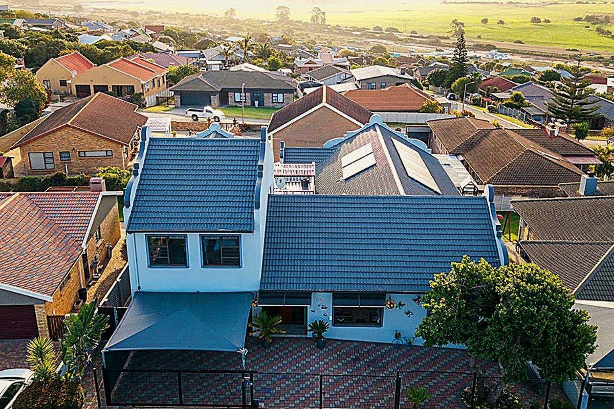 Aerial view of a residential property featuring a tiled roof with solar panels, a paved driveway, and a shade sail in a suburban setting.