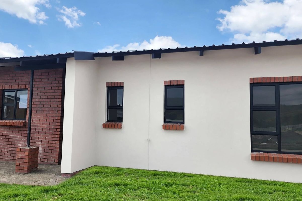 A well-maintained rear exterior view of the house featuring a combination of brick and plastered walls, modern aluminium windows, and a paved patio area.