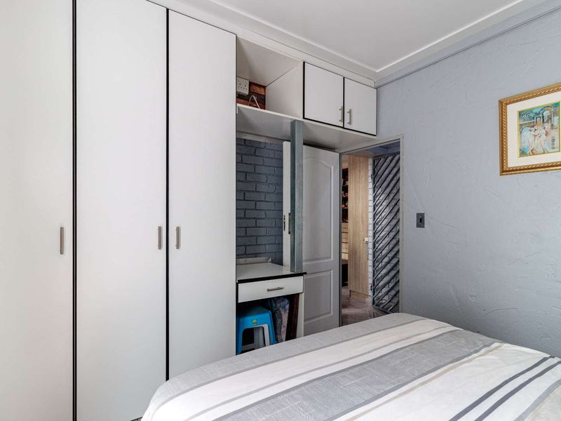 Bedroom featuring white built-in cupboards with overhead storage and a small integrated vanity desk, leading to an adjacent room via a security gate.