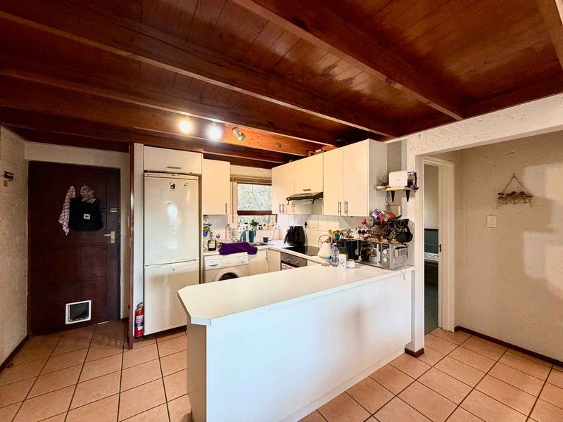 A functional kitchen featuring white cabinetry, a breakfast bar, tiled flooring, and exposed timber ceiling beams, offering a practical layout for daily use.