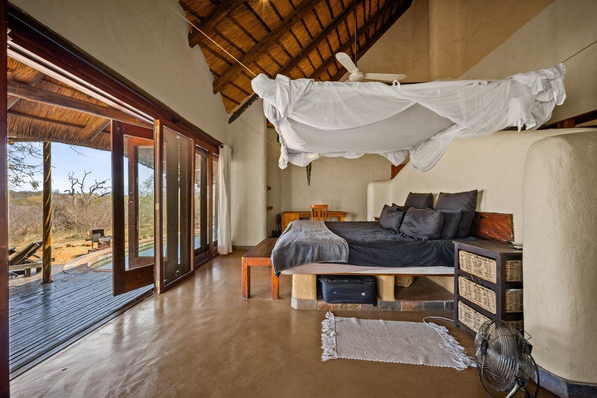 Spacious bedroom featuring a high thatched ceiling with exposed rafters, polished concrete floors, and large sliding doors opening onto a private deck.
