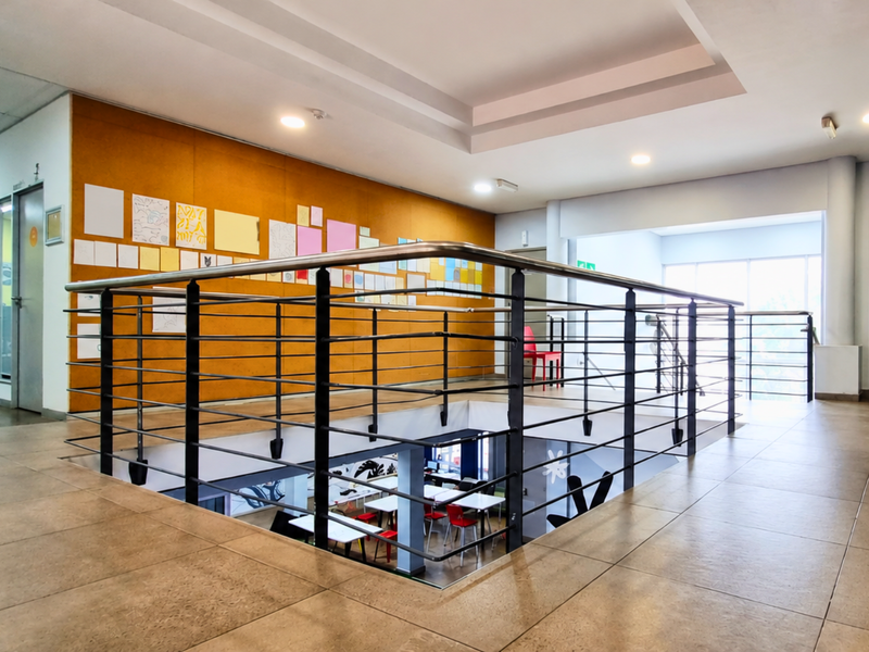A spacious office hallway featuring tiled flooring, a modern metal balustrade overlooking the lower level, and a large cork wall panel.