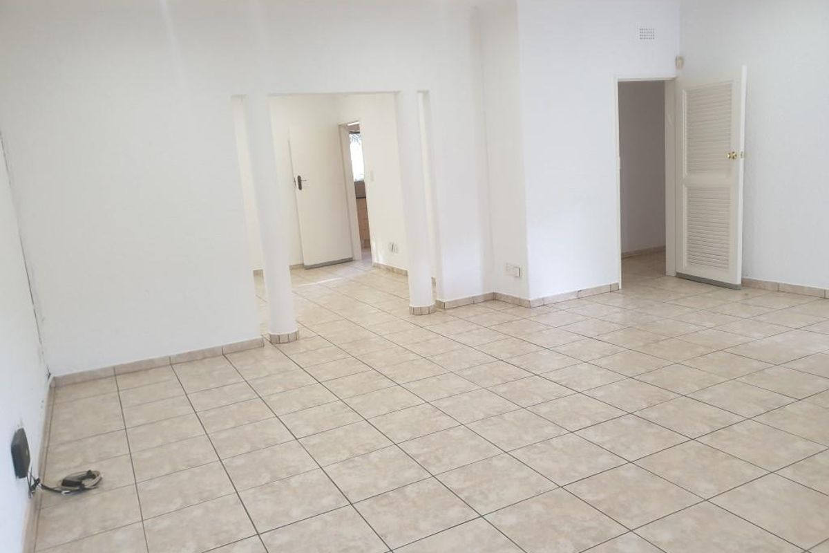 A spacious, empty living area featuring neutral tiled flooring, recessed lighting, and structural columns, providing a versatile blank canvas for interior design.