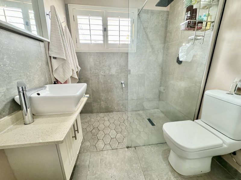 Modern bathroom featuring a walk-in shower with glass screen, vessel sink on a vanity cabinet, and neutral grey tiling throughout.
