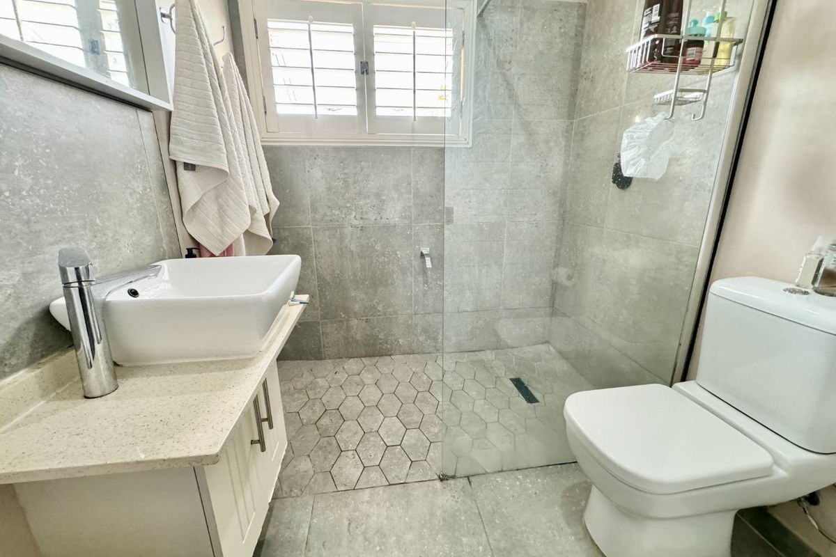 Modern bathroom featuring a walk-in shower with glass screen, vessel sink on a vanity cabinet, and neutral grey tiling throughout.