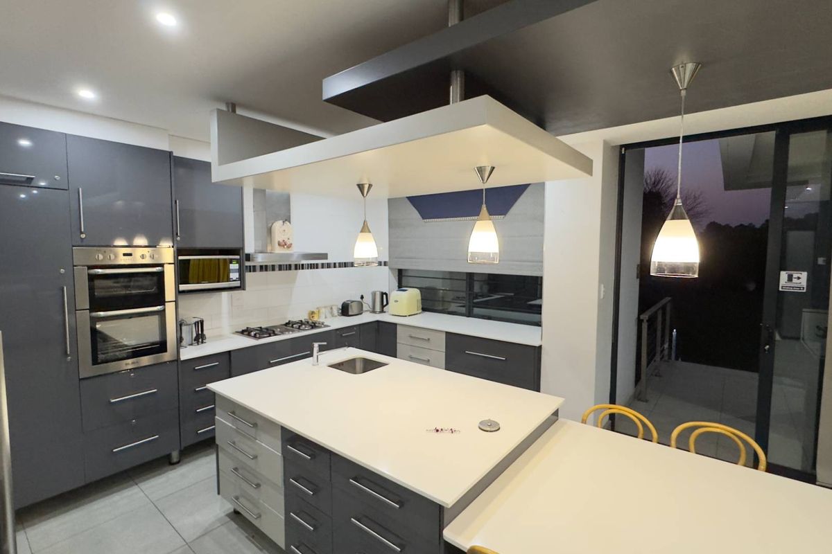 Modern kitchen featuring a central island with integrated sink, built-in double oven, gas hob, extractor fan, and sleek grey cabinetry with stone countertops.