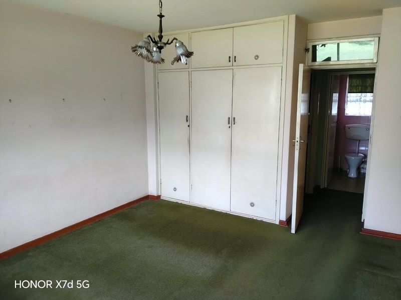 An empty bedroom featuring built-in cupboards, green carpet flooring, and a ceiling light fixture, with an adjacent view into a bathroom.