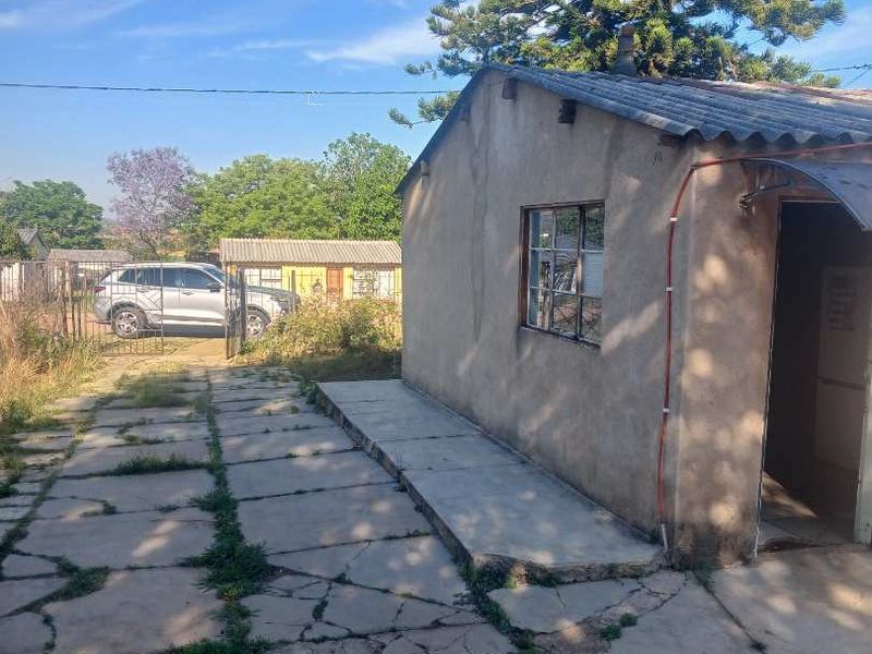 Rear exterior view of the property featuring a concrete paved area, corrugated roofing, and weathered wall finishes with visible signs of wear.