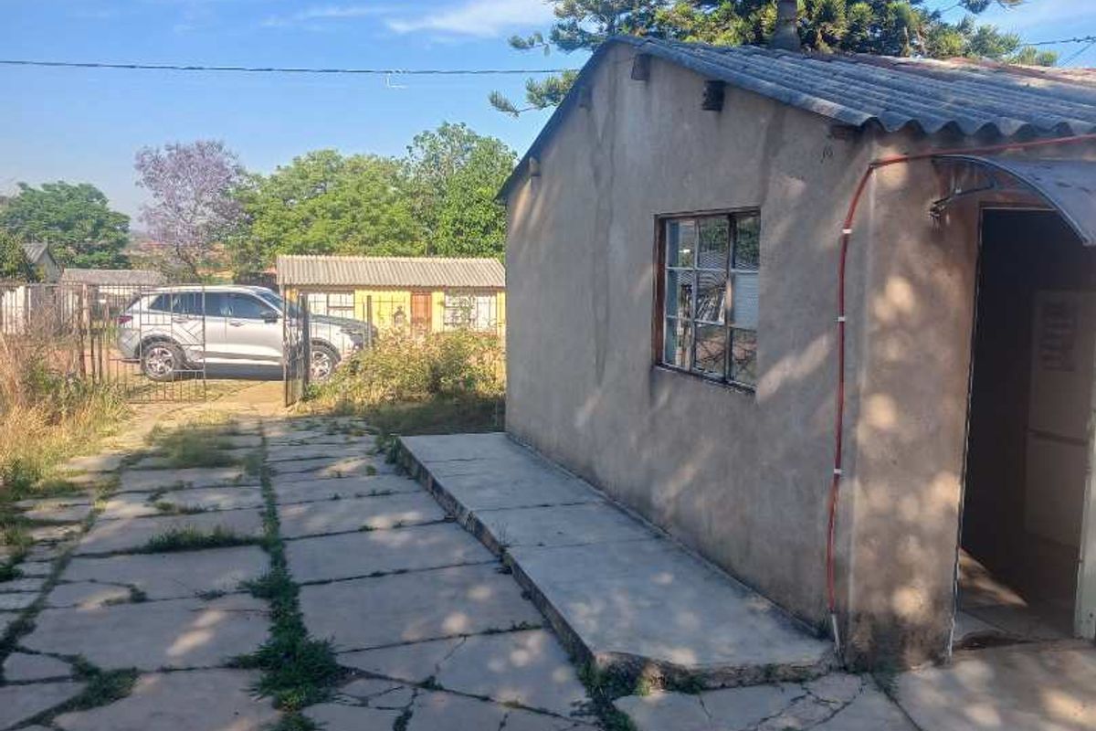 Rear exterior view of the property featuring a concrete paved area, corrugated roofing, and weathered wall finishes with visible signs of wear.