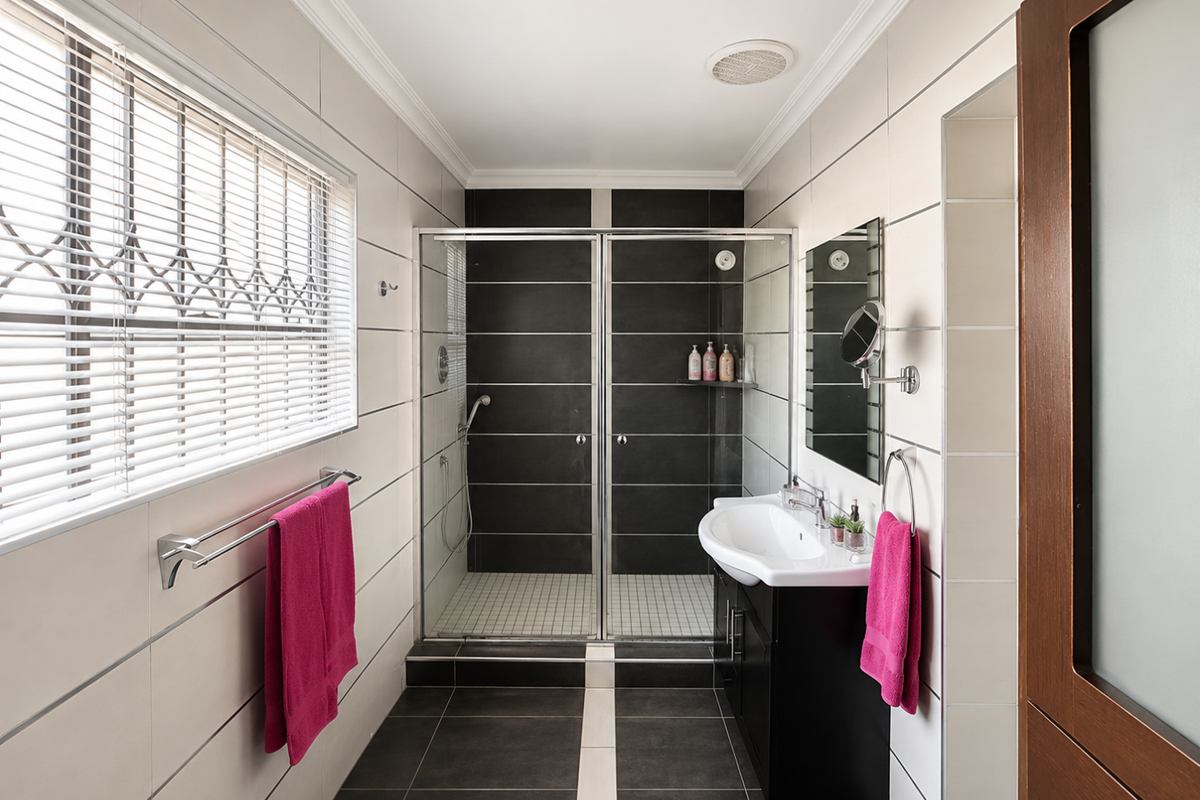 Modern bathroom featuring a walk-in shower with dark tiled accents, a sleek vanity cabinet with basin, and neutral wall tiling.