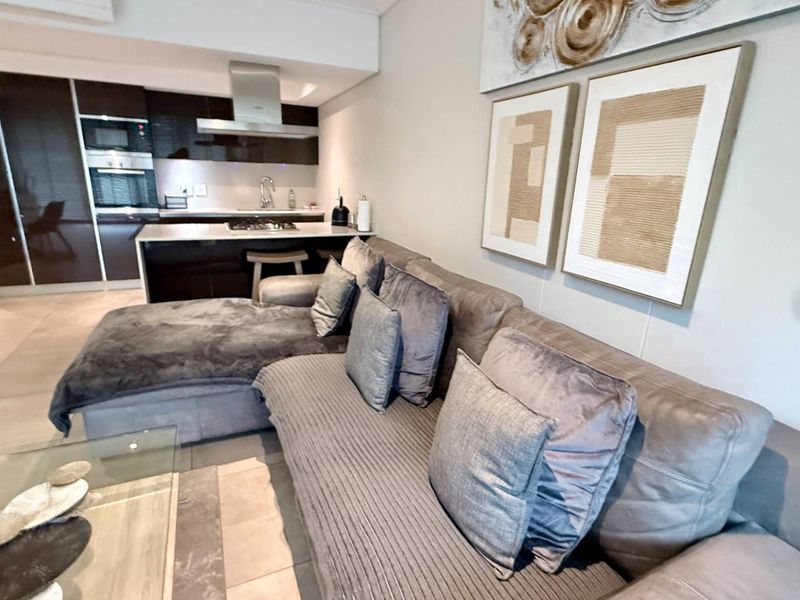 Modern open-plan living area featuring a sleek kitchen with built-in cabinetry, stainless steel appliances, and a central island, seamlessly flowing into the lounge space.