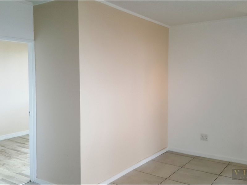 A bright, empty bedroom featuring neutral wall tones, tiled flooring, and a window with fitted blinds, offering a clean and versatile living space.