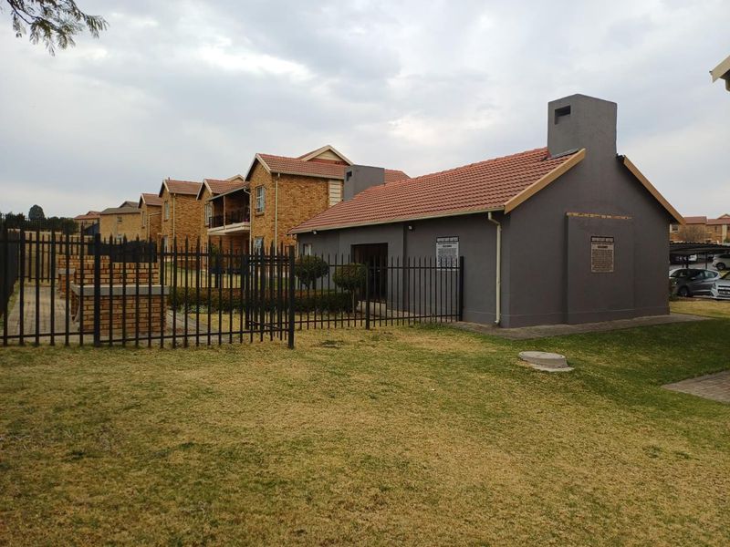 Exterior view of the apartment complex grounds featuring a communal brick braai area, manicured lawn, and secure metal perimeter fencing.