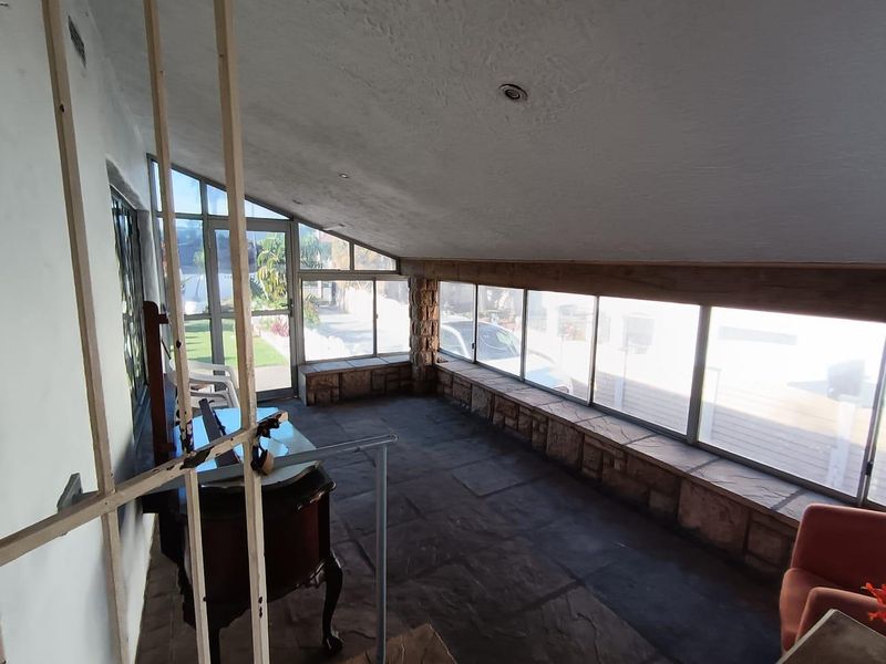 Enclosed patio area featuring stone flooring, stone-clad window sills, and extensive glazing, offering a bright and versatile space with potential for modern updates.