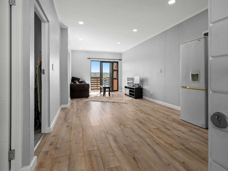An open-plan living area featuring modern laminate flooring, recessed downlighting, and a sliding glass door leading to a balcony with scenic views.