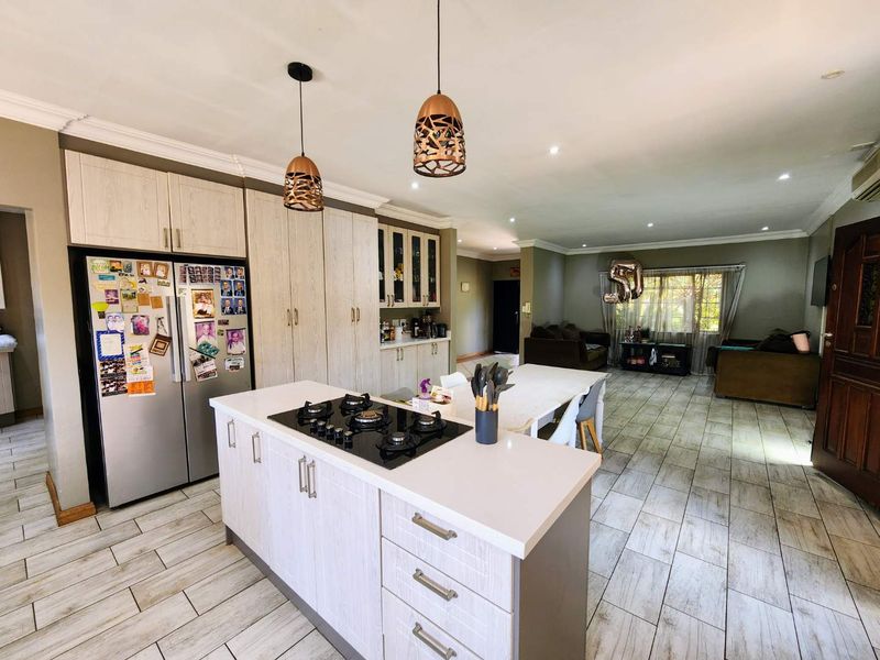 Spacious open-plan living area featuring a modern kitchen with a central island, gas hob, stone countertops, and contemporary pendant lighting throughout.