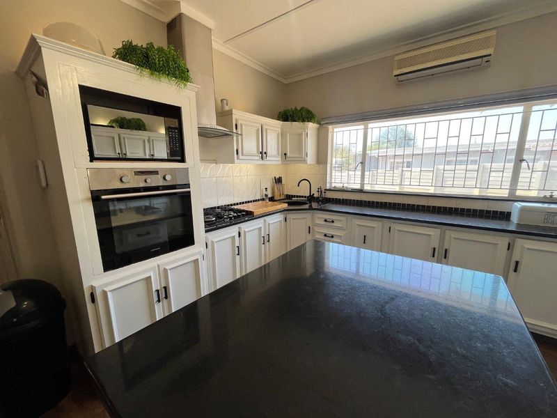 A well-maintained kitchen featuring white cabinetry, black granite countertops, a central island, built-in oven, microwave, and a gas hob with an extractor fan.
