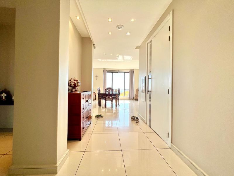 A bright, modern hallway featuring large format polished floor tiles and recessed downlighting, leading towards an open-plan living and dining area.