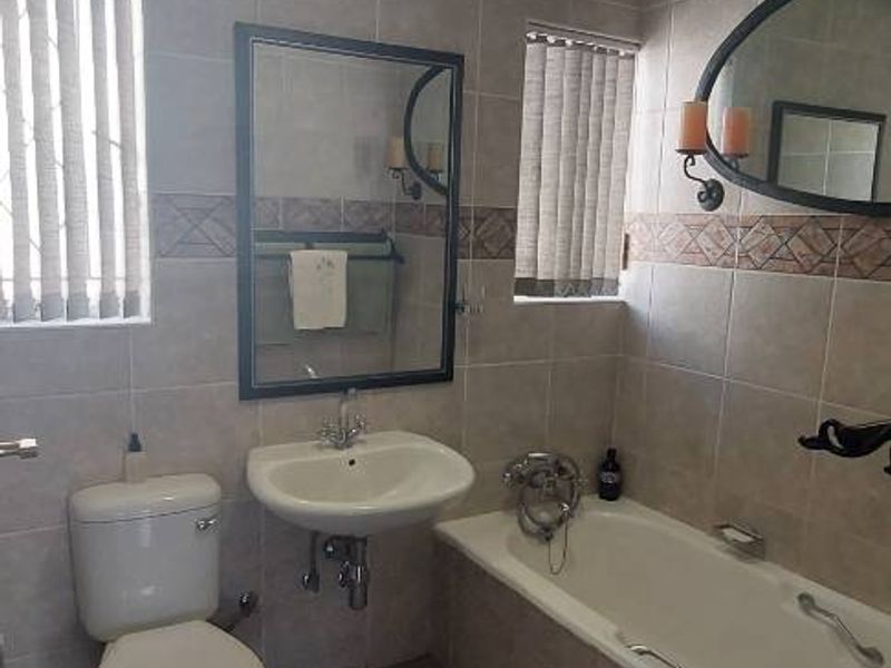 A functional bathroom featuring ceramic wall and floor tiling, a pedestal basin, a standard toilet, and a bathtub with a shower mixer.