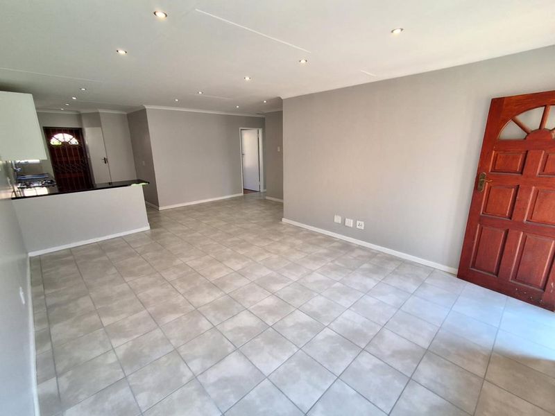 An open-plan living area featuring neutral tiled flooring, recessed downlights, and a functional kitchen space with granite countertops.