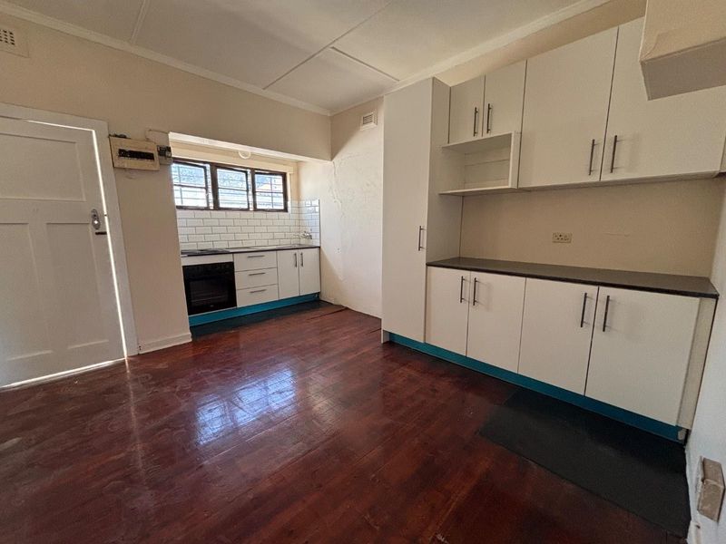 A functional kitchen featuring white built-in cabinetry, subway tile backsplash, built-in oven, and timber flooring, offering a clean canvas for potential updates.