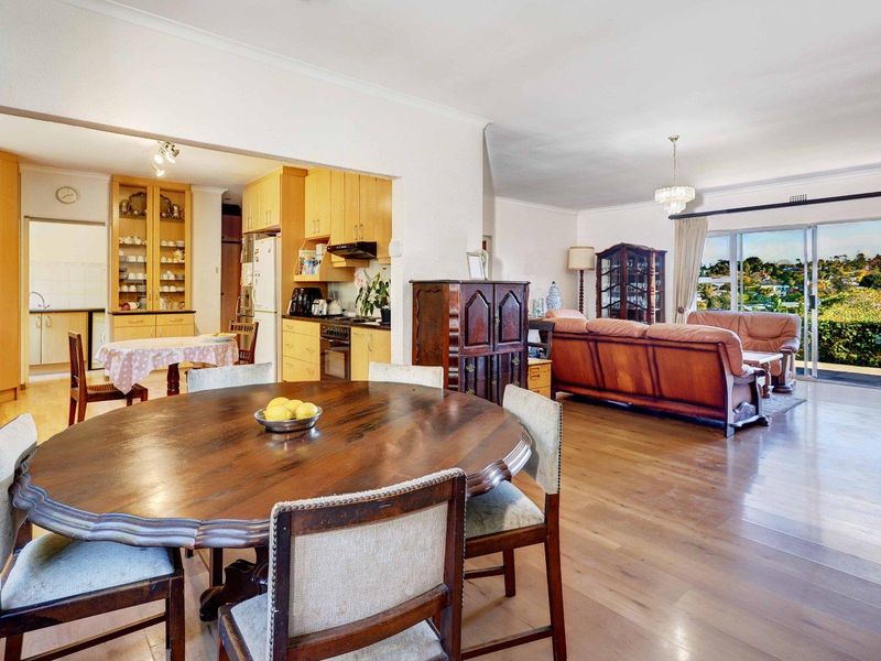 Spacious open-plan living and dining area featuring timber flooring, integrated kitchen cabinetry, and large sliding doors leading to an outdoor view.