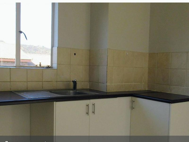 A functional kitchen area featuring built-in cabinetry, a stainless steel sink, and tiled backsplash, currently vacant and ready for updates.