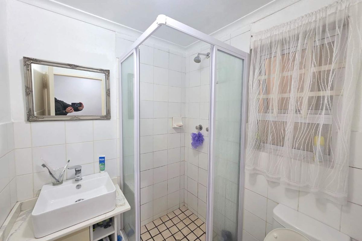 A functional bathroom featuring a corner shower enclosure, a modern basin, and a toilet, with white wall tiling and a window for natural light.