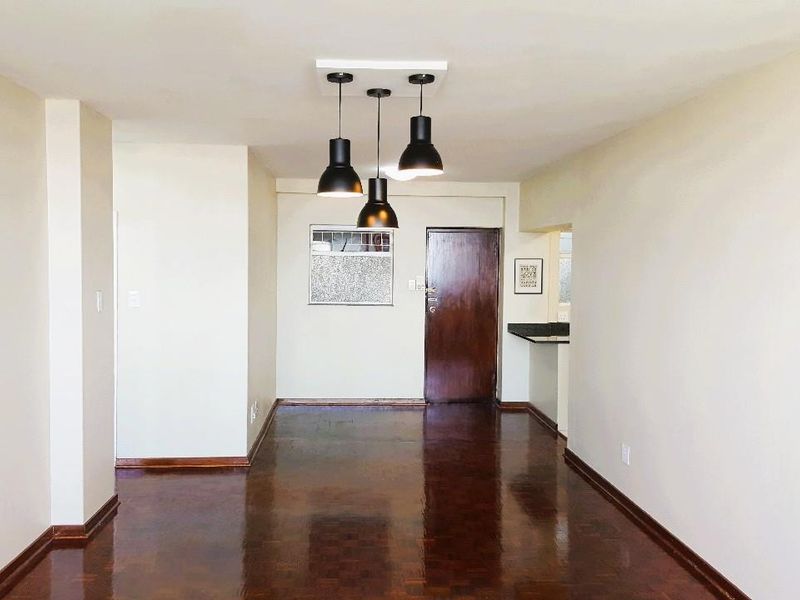 A bright, open-plan living area featuring polished parquet flooring, modern pendant lighting, and a convenient kitchen pass-through window.